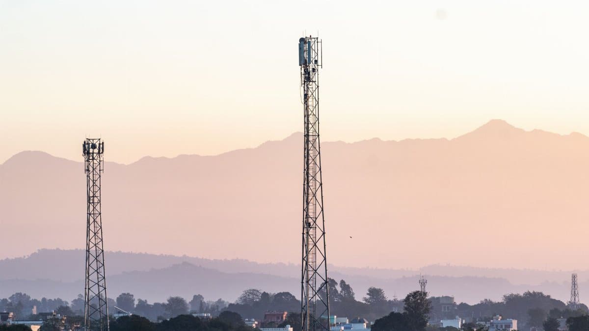 Telecom towers rise above a town against a backdrop of mountains at dawn, highlighting communication infrastructure.