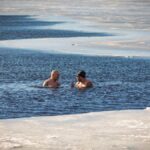 Two men brave the cold for a swim in a partially frozen lake during winter.