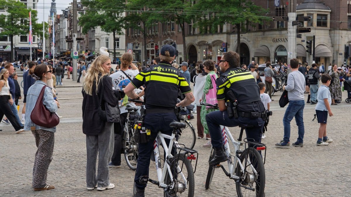 Police officers on bicycles interact with people in a bustling city square scene.