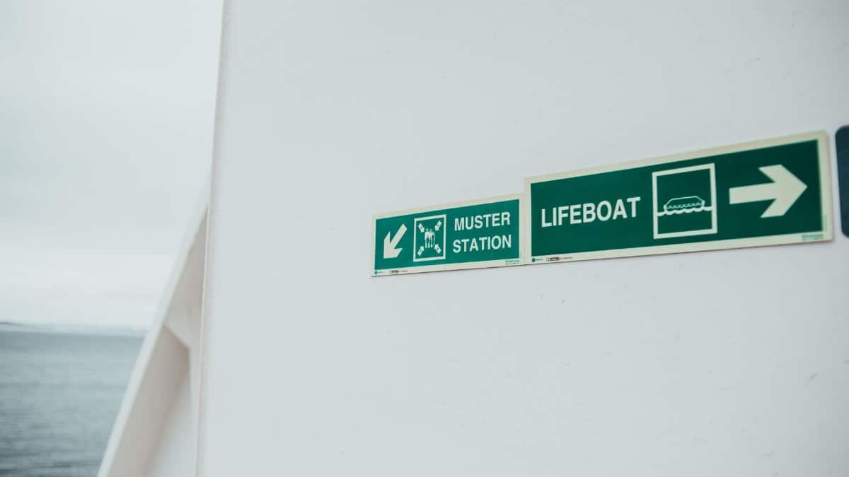 Close-up of muster station and lifeboat signs on a ship's exterior wall, guiding passengers to safety.