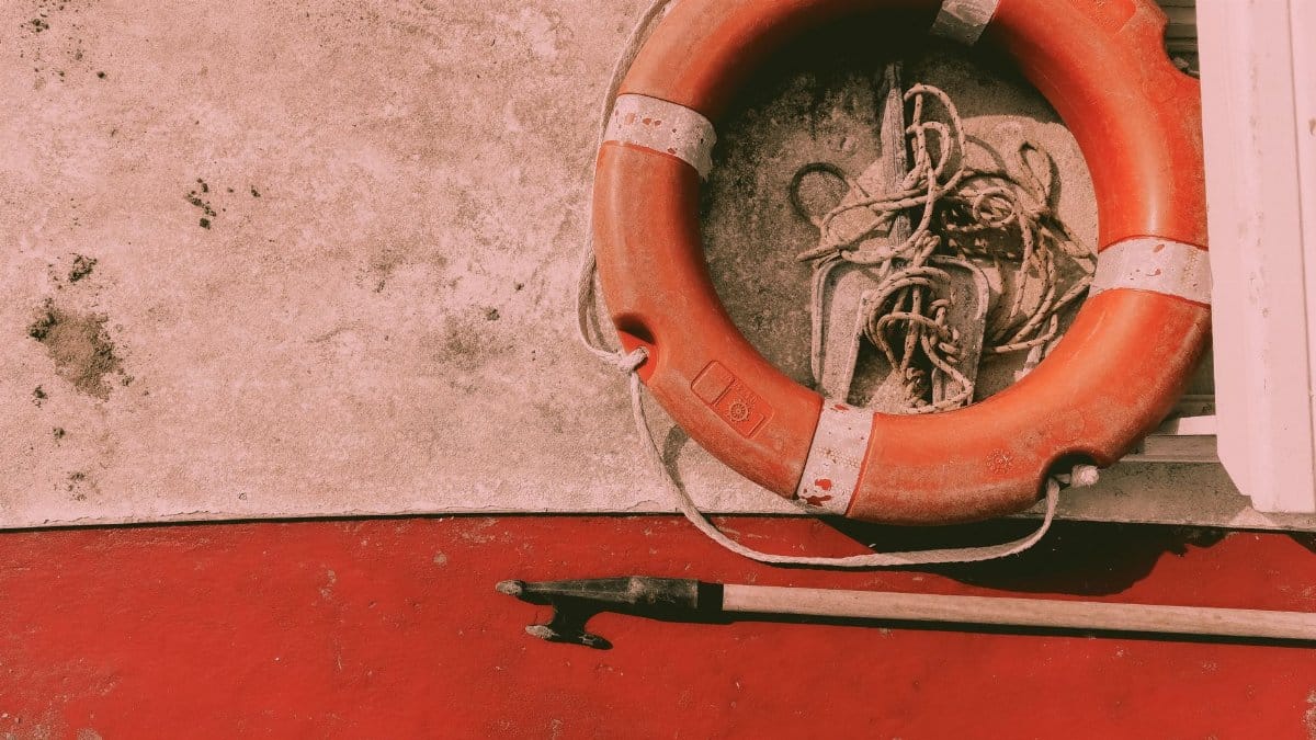 Close-up of a vintage lifesaver ring tied with rope on a red boat deck, suggesting maritime safety.