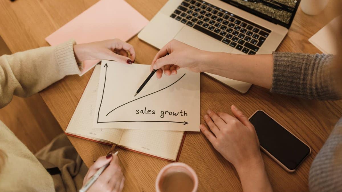 Two women plan sales growth with graphs and technology in an office setting.