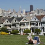 A woman reads in a park with San Francisco's iconic skyline and Painted Ladies in the background.