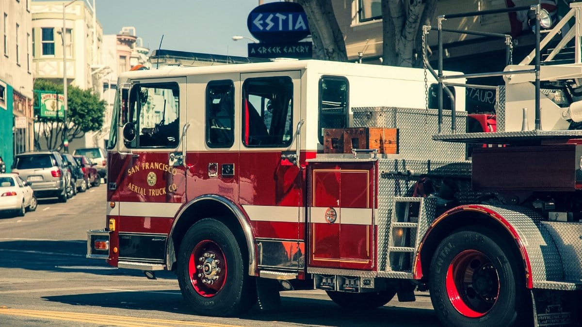 A vibrant red San Francisco fire truck navigates a bustling city street in daylight.