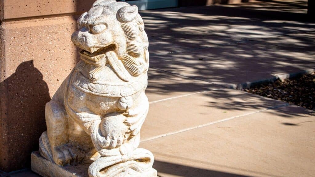 A detailed stone sculpture of a Chinese guardian lion on a sunny sidewalk in Washington, UT.