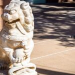 A detailed stone sculpture of a Chinese guardian lion on a sunny sidewalk in Washington, UT.