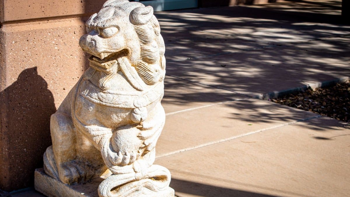 A detailed stone sculpture of a Chinese guardian lion on a sunny sidewalk in Washington, UT.