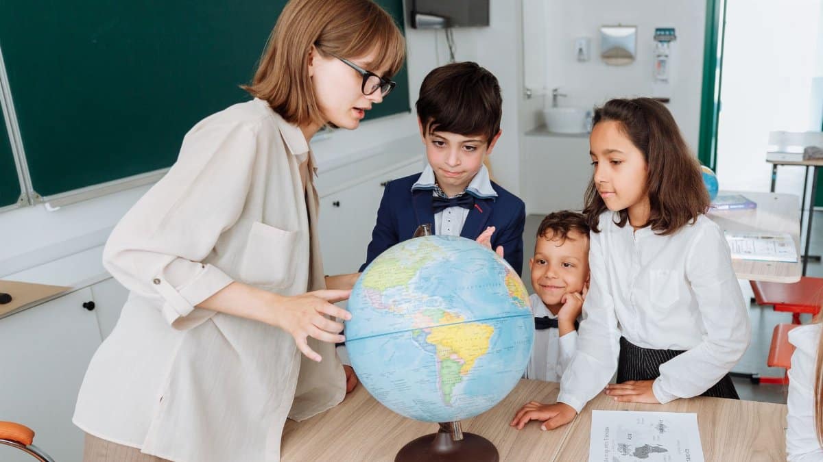 A teacher and three students engaged in a geography lesson, examining a globe in a classroom setting.