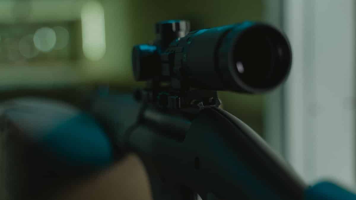 Focused image of a rifle with a mounted scope in a controlled environment.