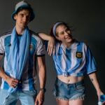 Two young fans in Argentina soccer apparel pose with enthusiasm indoors.