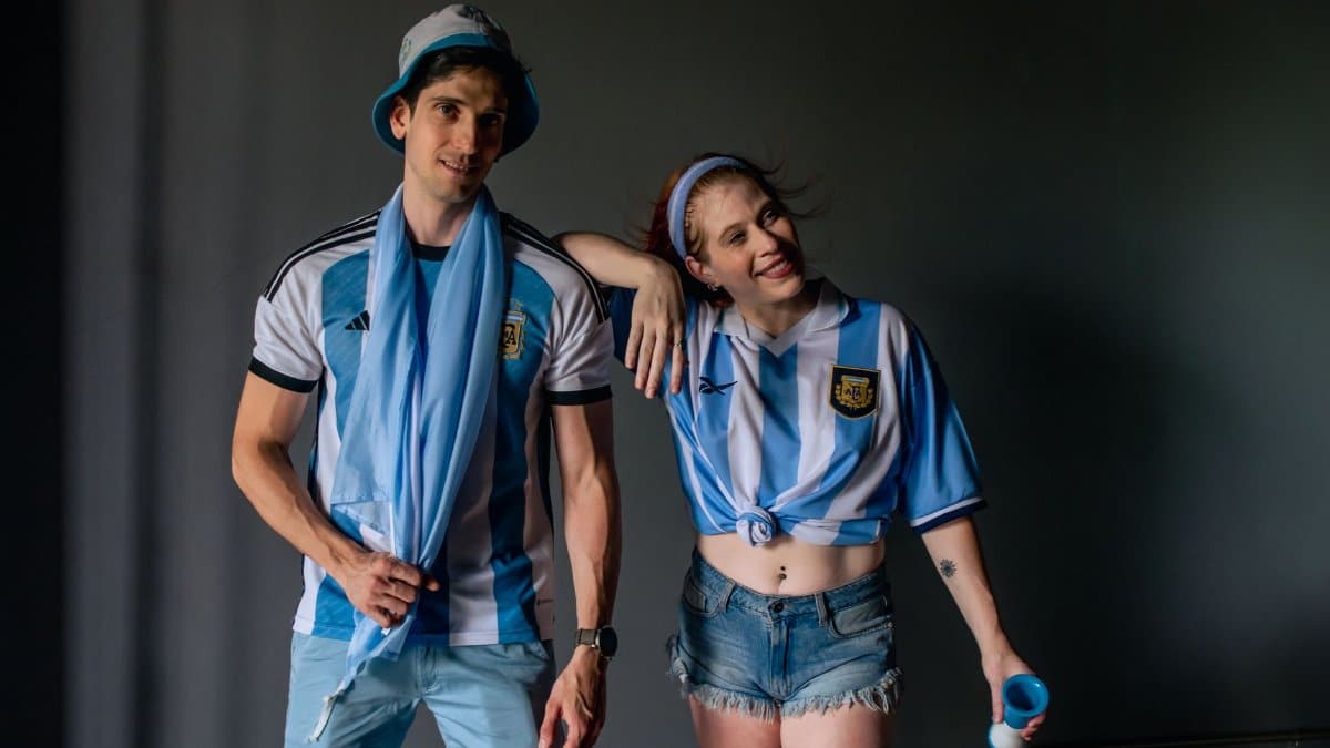Two young fans in Argentina soccer apparel pose with enthusiasm indoors.