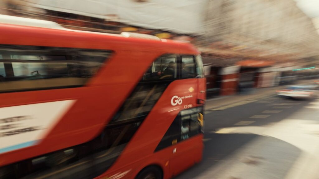 Blurred motion of a classic red London bus speeding through a busy street, capturing city life energy.