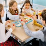 Group of diverse children having lunch in a school canteen, sharing and enjoying healthy snacks.