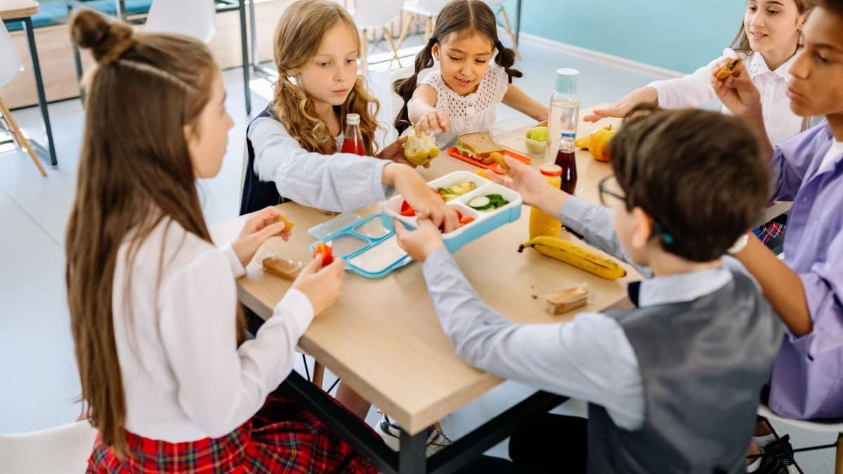 Group of diverse children having lunch in a school canteen, sharing and enjoying healthy snacks.