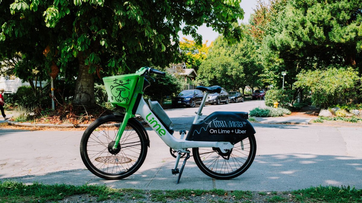 Lime bike parked on a sunny street in Seattle, offering a green transportation option among lush trees.