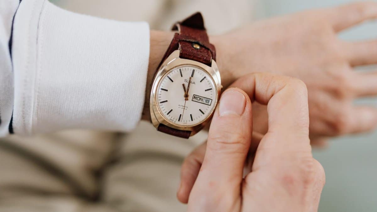 A close-up of a person adjusting a vintage brown leather strap analog wristwatch.