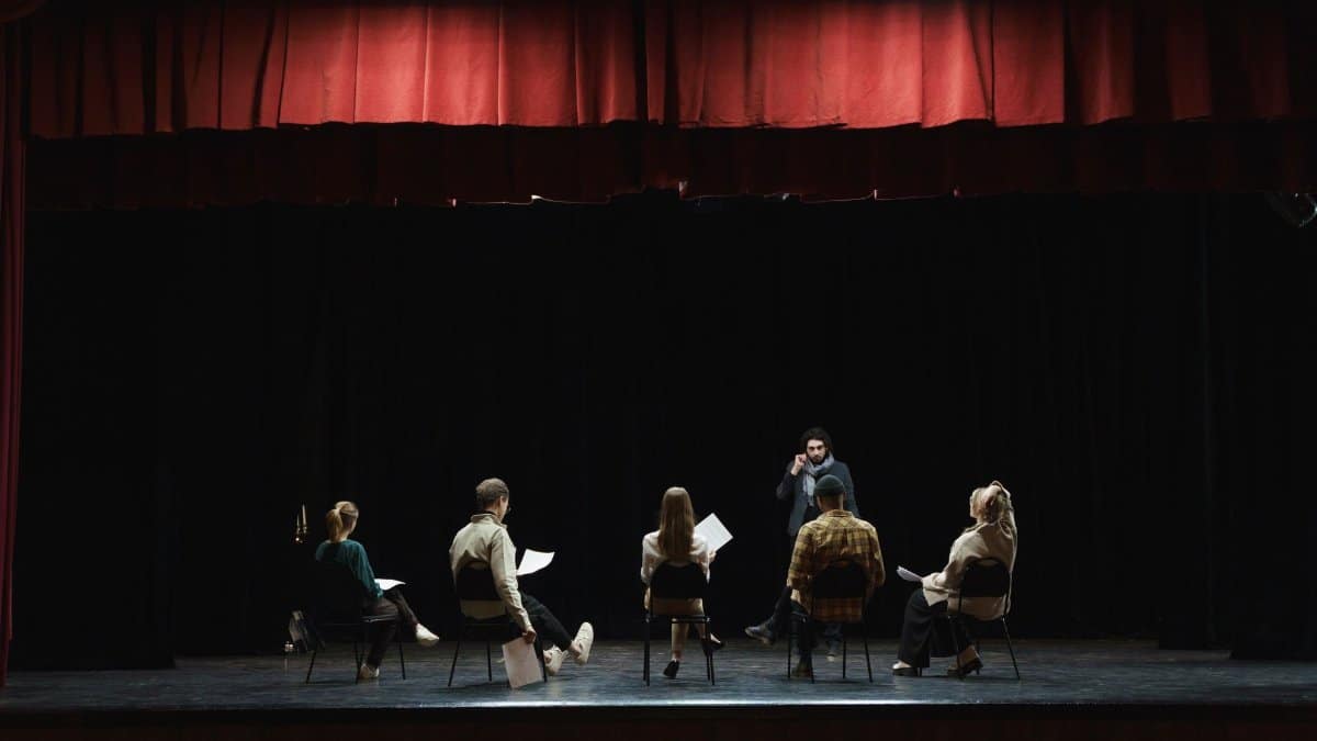 A group of actors rehearsing on a dimly lit stage in an auditorium, preparing for a theater performance.