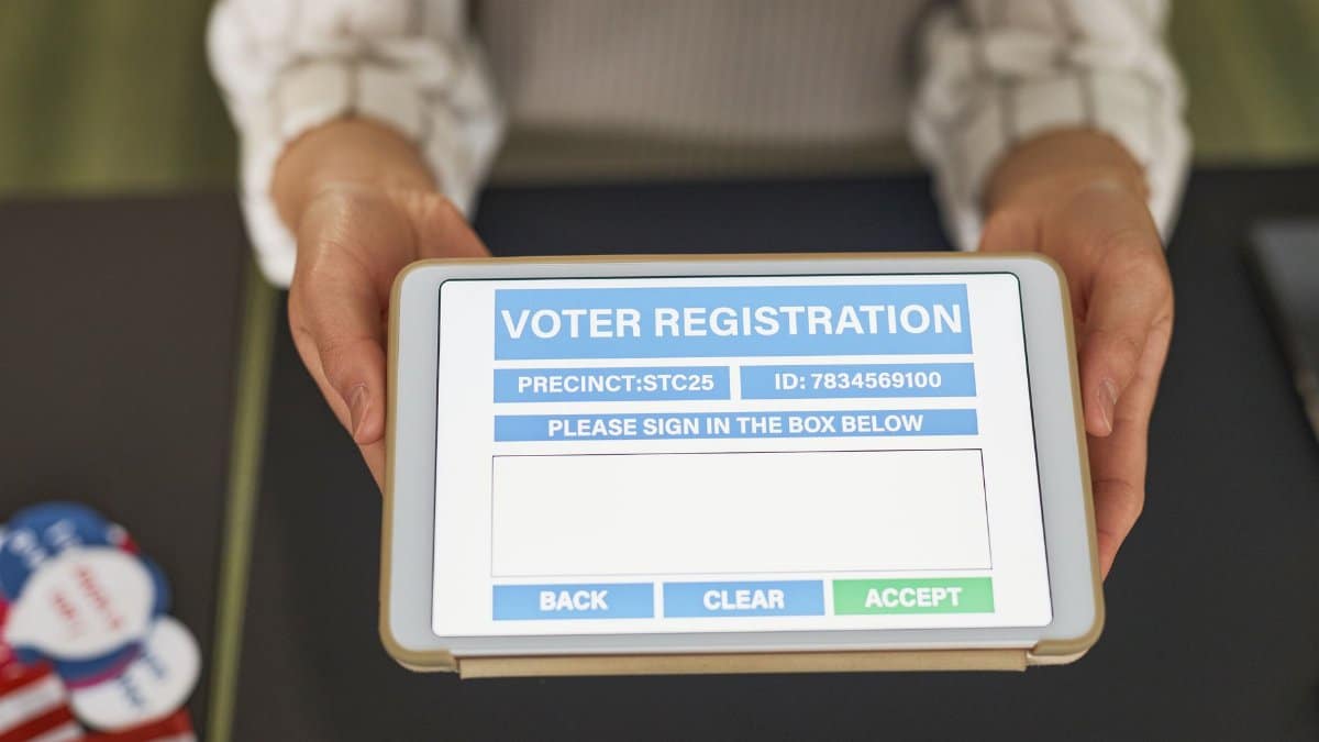 Close-up of hands holding a tablet displaying digital voter registration form.