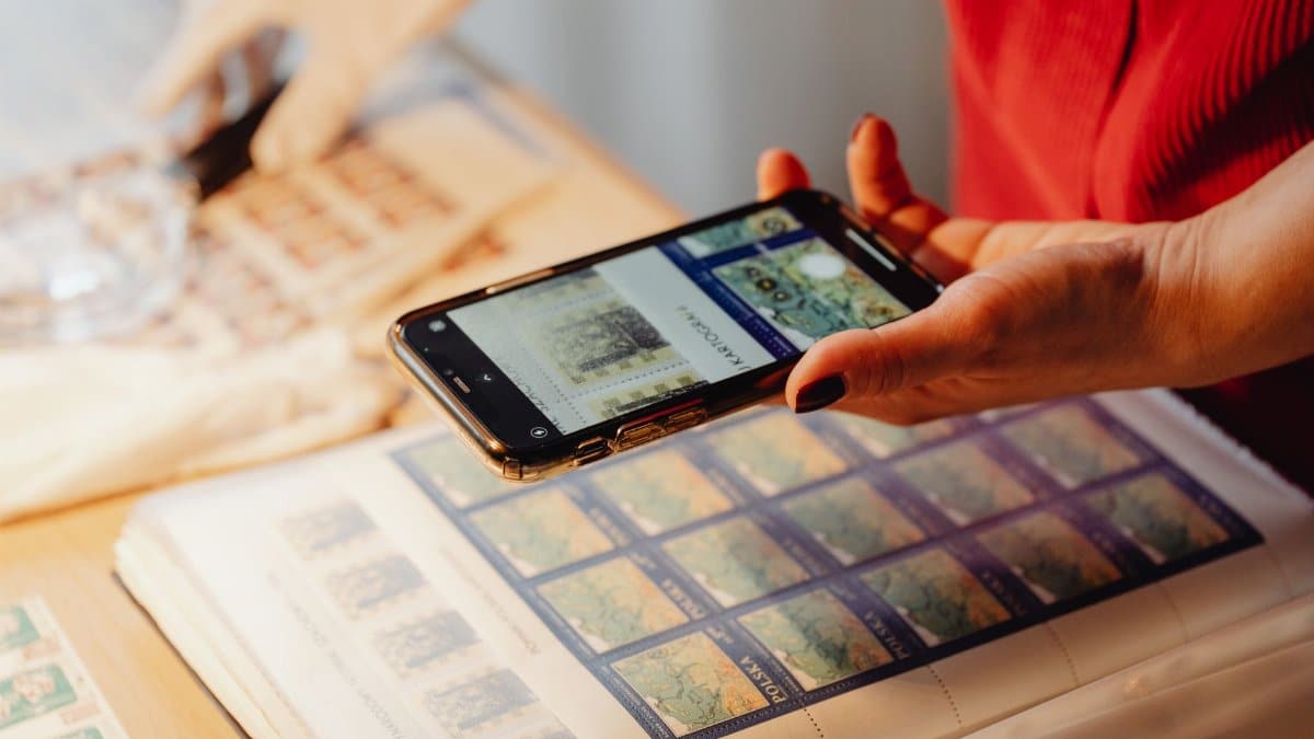 Individual photographing a stamp collection using a smartphone for cataloging.