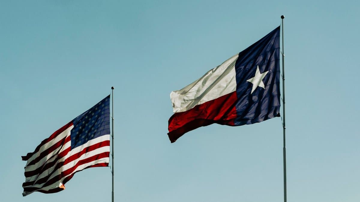 American and Texas flags waving under a clear blue sky, symbolizing patriotism and freedom.