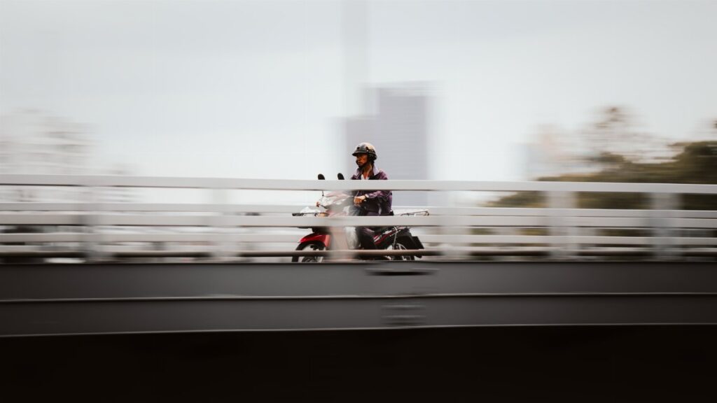 A motorcyclist rides across a bridge in Bangkok with a dynamic motion blur effect.