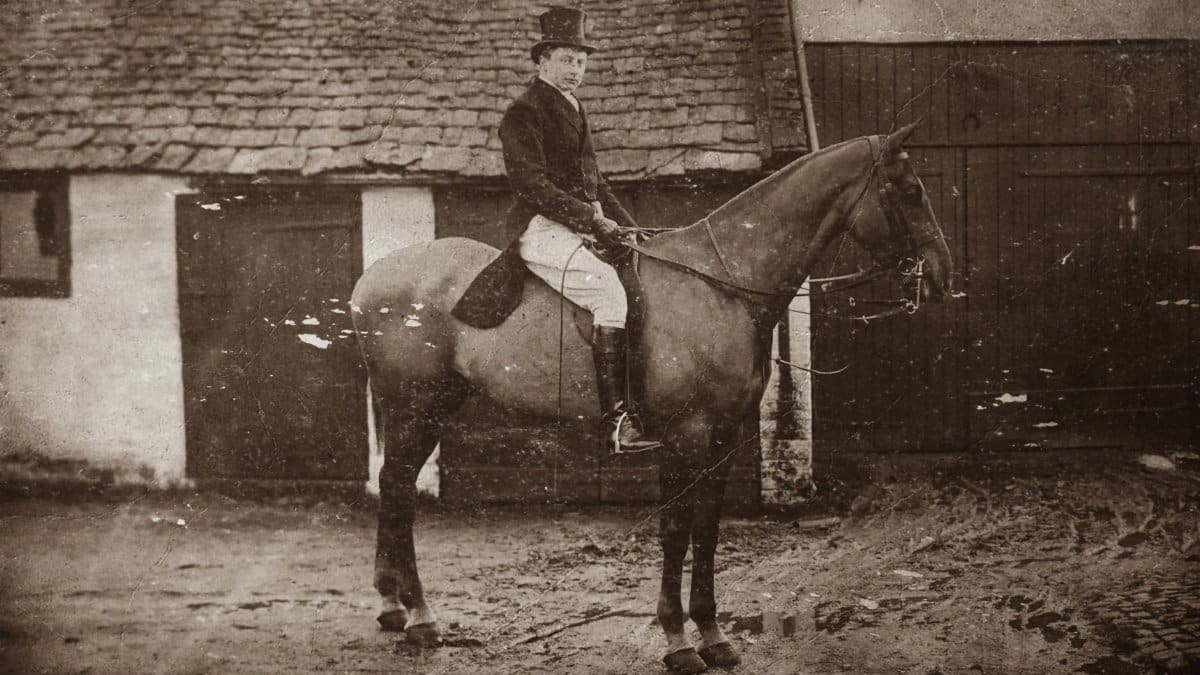 A sepia-toned classic portrait of a man riding a horse in a rural setting.