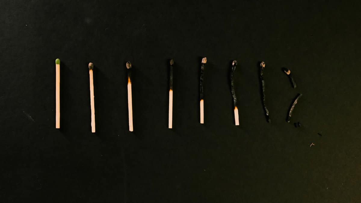 Progression of matches from unburnt to fully burnt on a dark surface, reflecting decay and transformation.