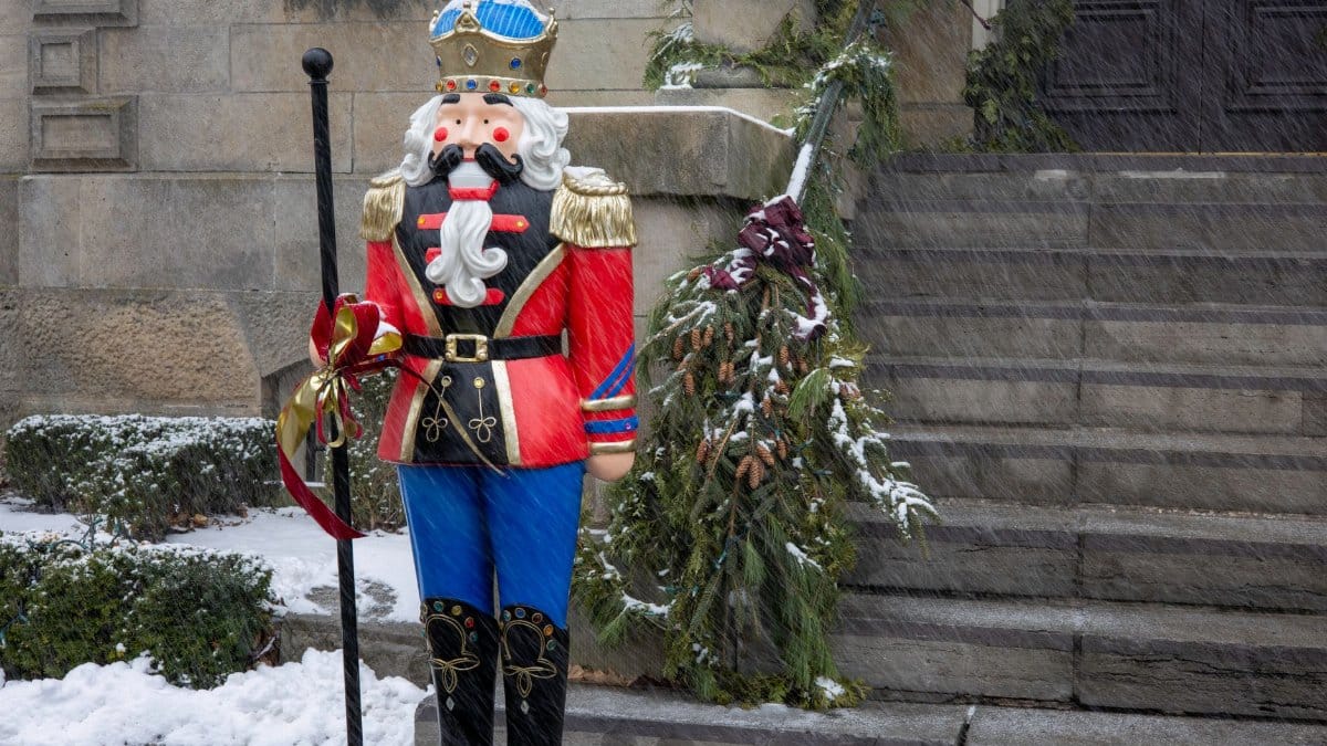 Colorful nutcracker statue in winter setting, adorned with holiday decorations and surrounded by snow.
