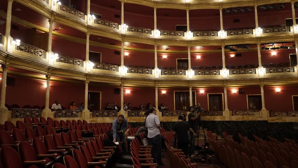 View of a classic theater interior with red seats and a camera crew setting up, capturing the venue's grandeur.