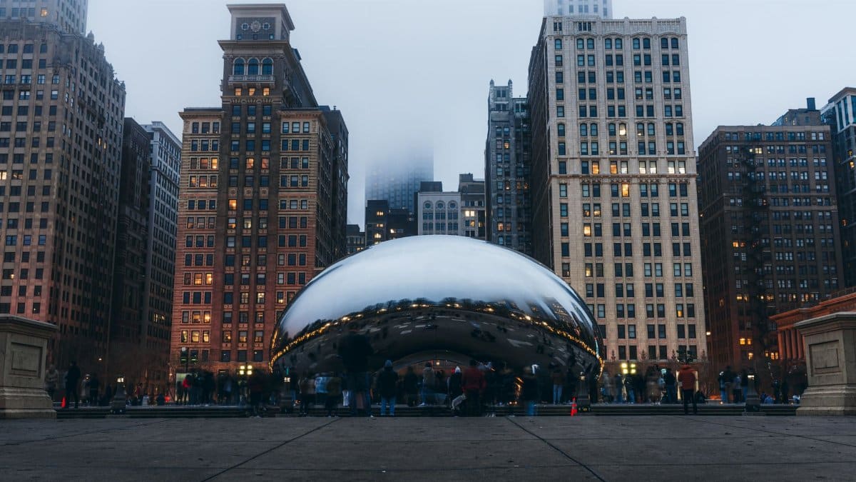 View of Cloud Gate in Chicago with skyscrapers and fog at dusk, creating a reflective urban scene.