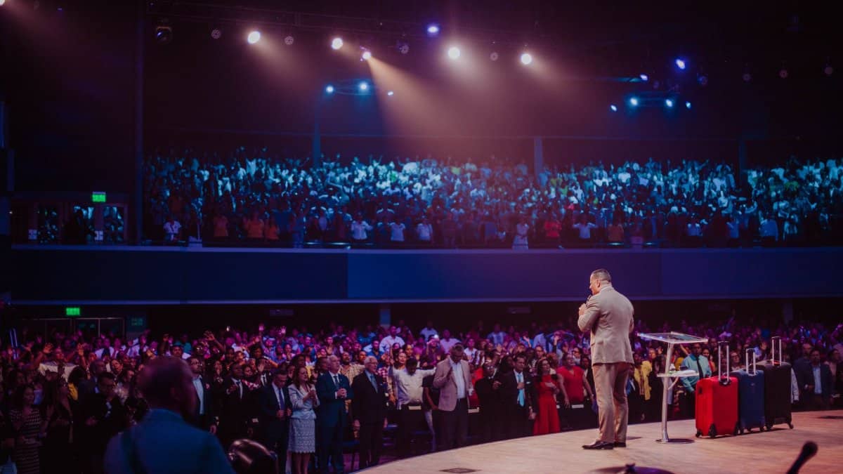 A speaker in a gray suit captivates a large crowd on stage during a motivational event.