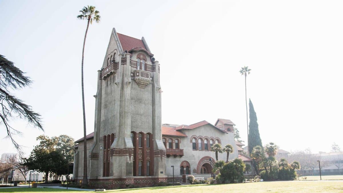 Tower Hall at San Jose State University amid palm trees under a bright summer sky.