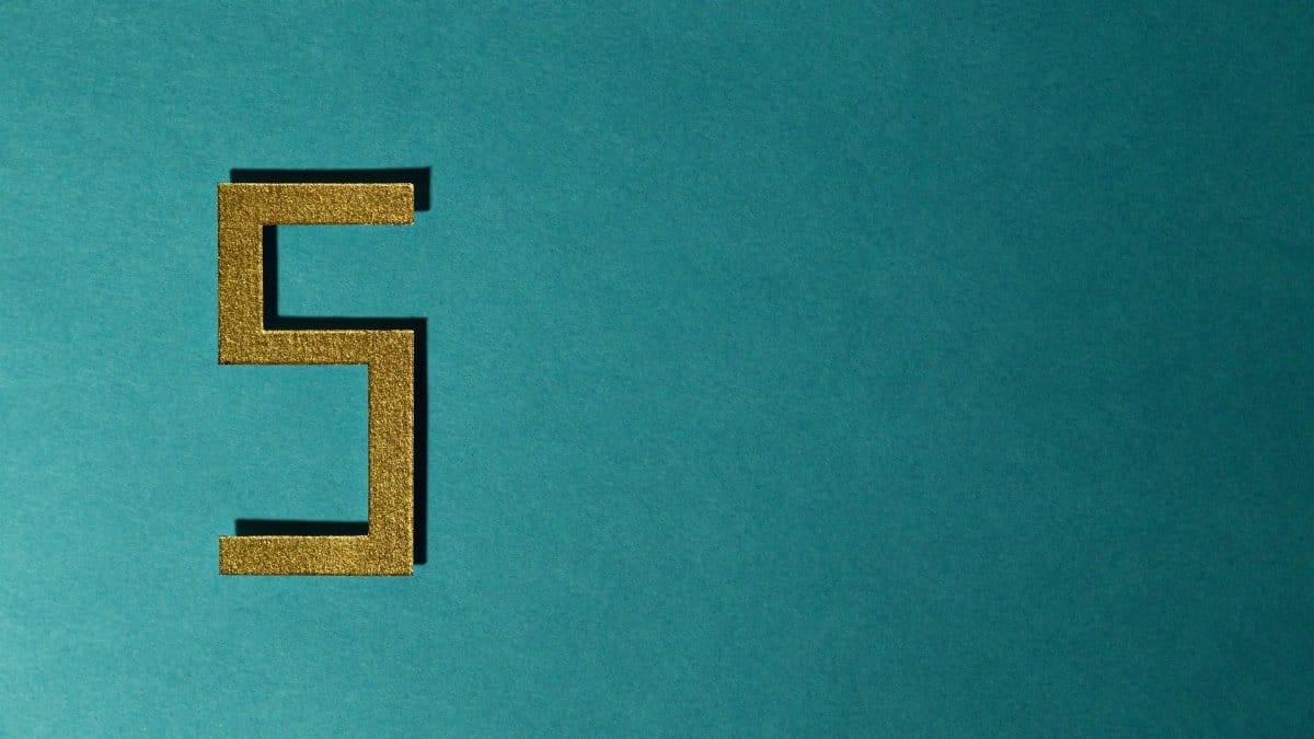 Abstract photo featuring a golden number five on a teal background with negative space.