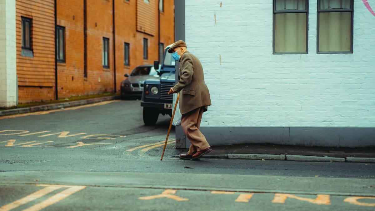 Senior man with cane walking past brick building on urban sidewalk.