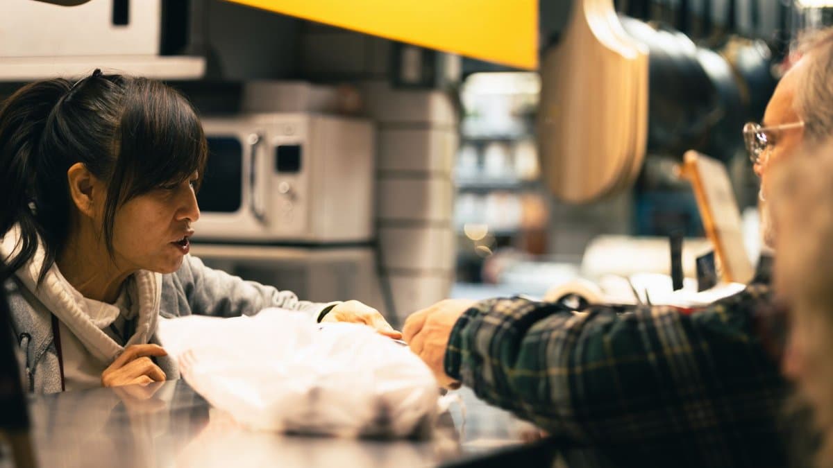 A vendor hands over a product to a customer at a bustling market counter.