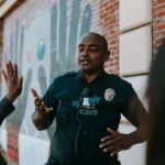 Police officer conversing with people on the street near a brick wall mural.