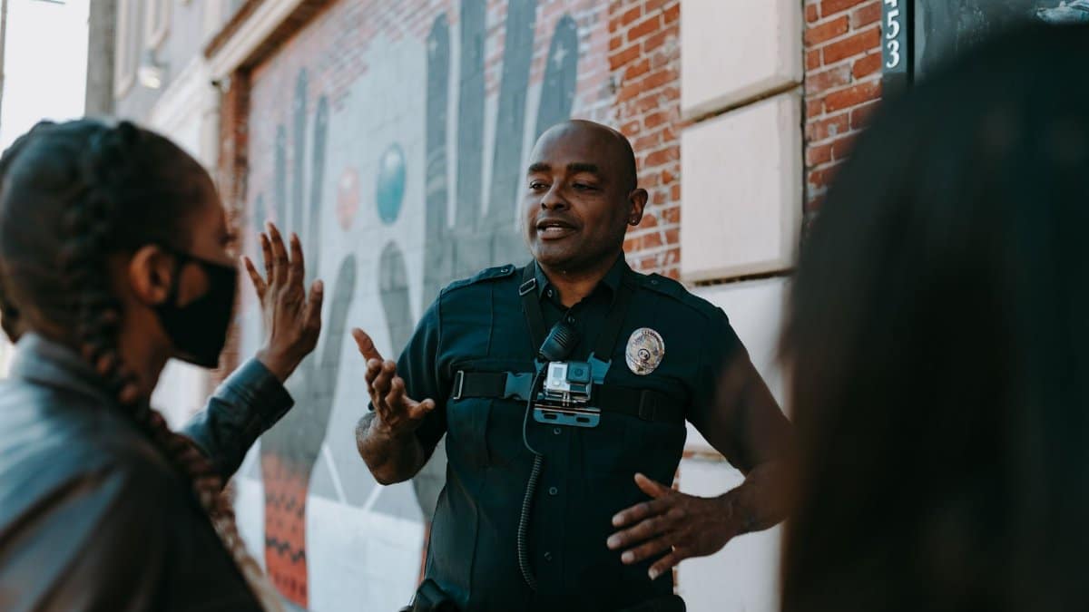 Police officer conversing with people on the street near a brick wall mural.