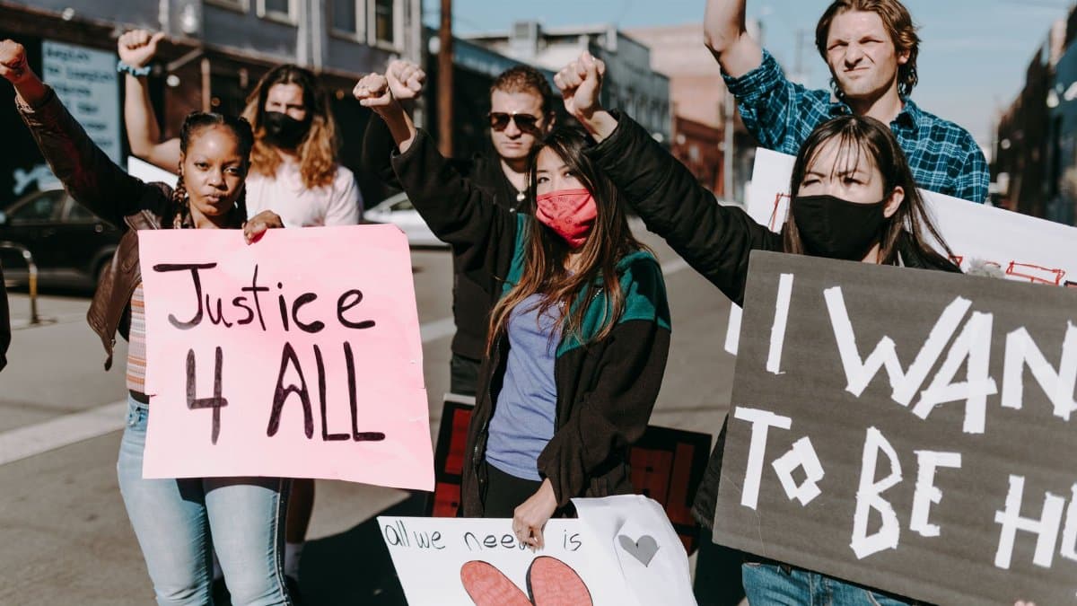 A diverse group of masked protesters holding signs for justice during an outdoor protest.
