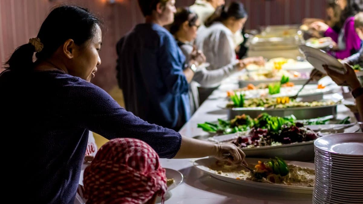 A diverse group of people enjoying a buffet dinner indoors with various dishes.