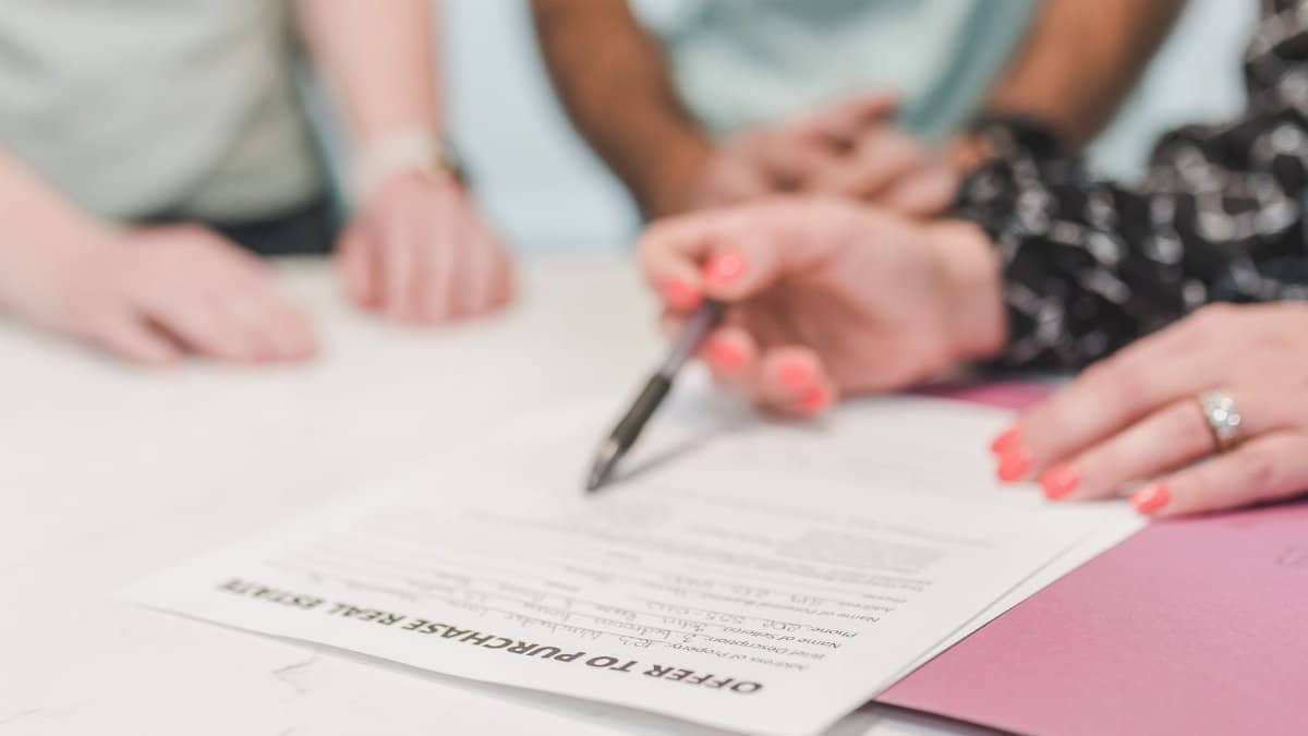 Close-up of people reviewing and signing an offer to purchase real estate document.