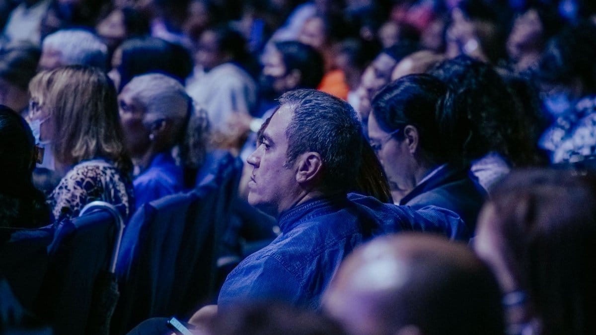 A large, diverse audience attentively listens during an indoor event.