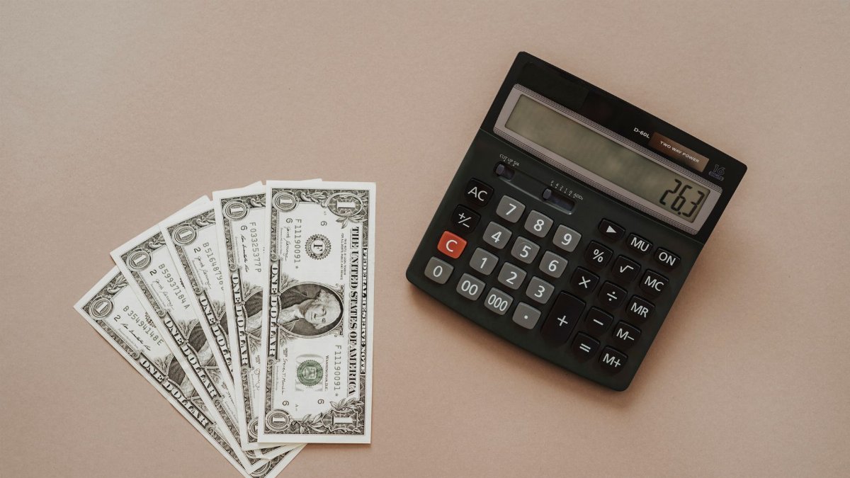 A calculator displaying '26.3' beside four one-dollar bills on a beige background.