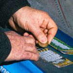 Hands using a coin to scratch off a lottery ticket on a blue table.