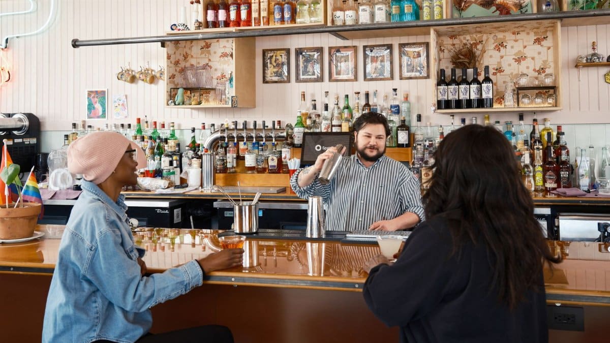 Bartender skillfully serves cocktails at a vibrant bar with guests enjoying the atmosphere.