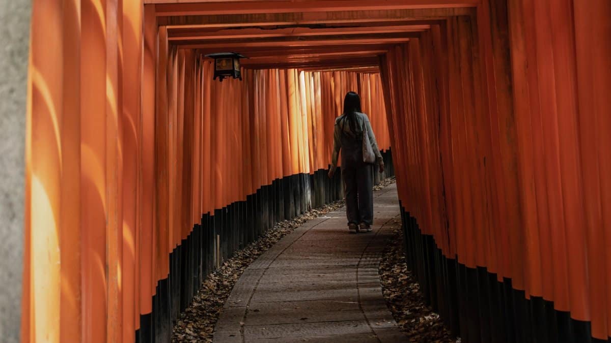 A woman walks through the iconic orange torii gates at Fushimi Inari Taisha in Kyoto, Japan, highlighting its cultural beauty.