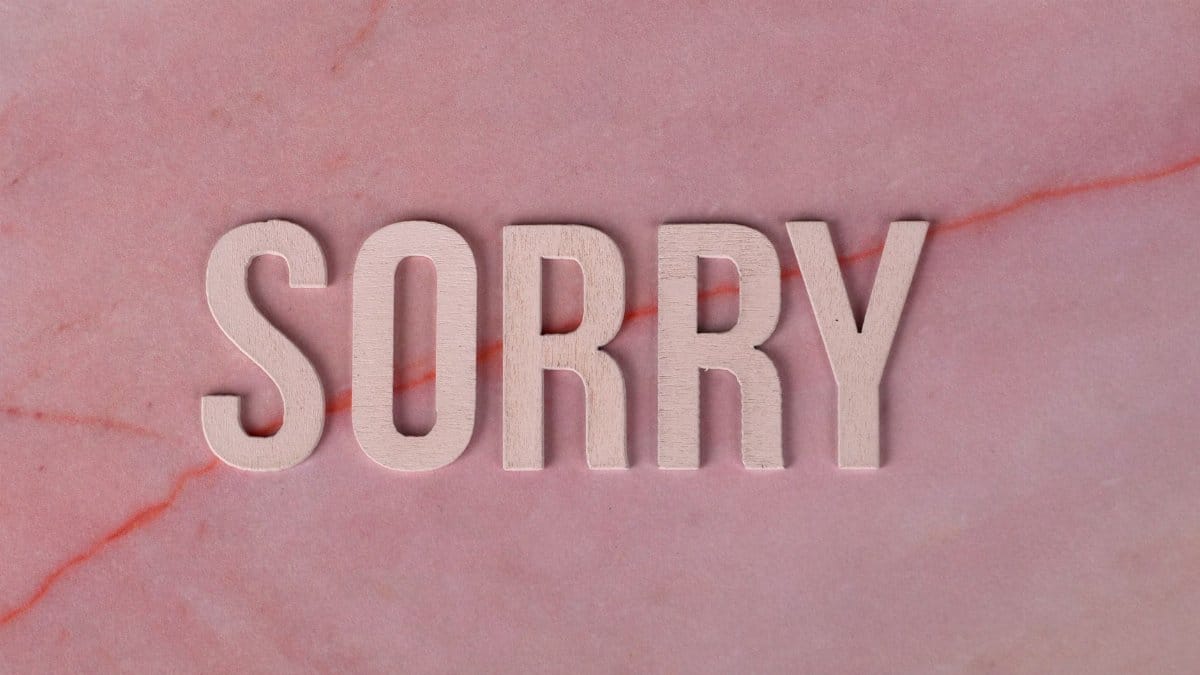 Wooden letters spelling 'SORRY' on a pink marble surface, apology concept.