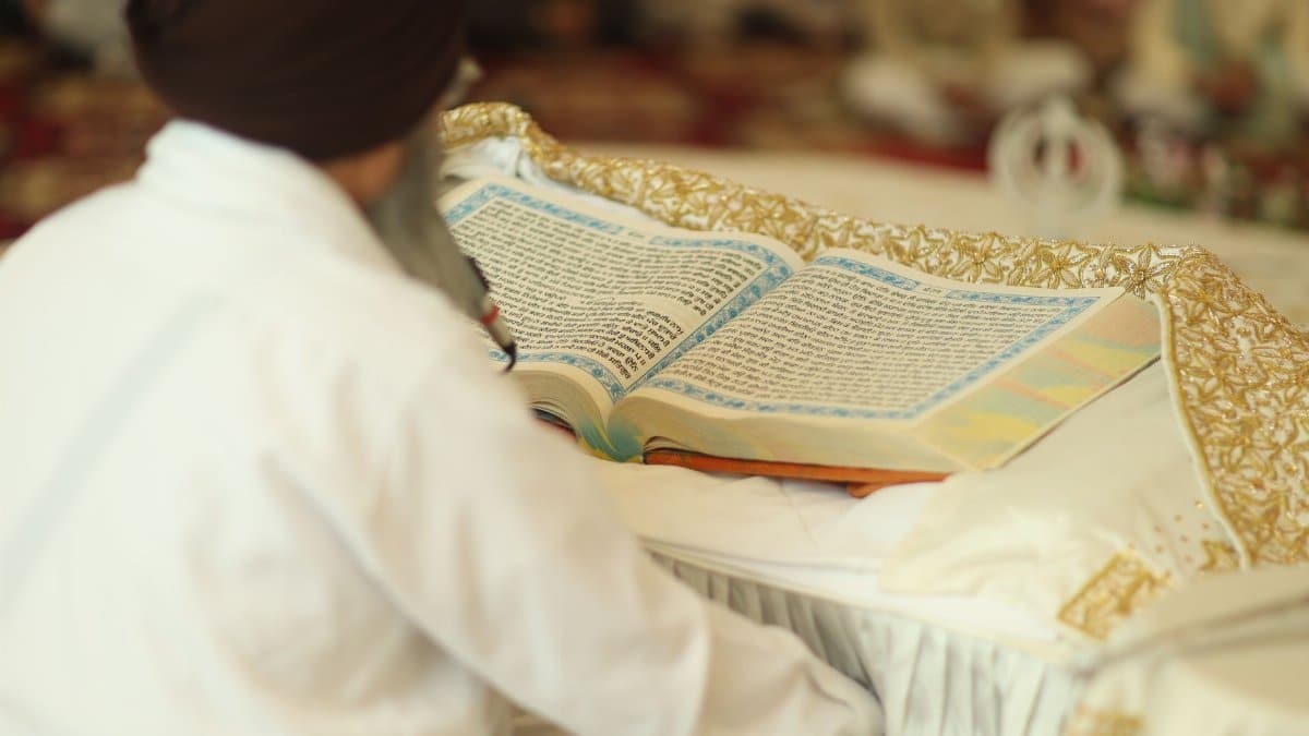 A Sikh devotee reading the Guru Granth Sahib inside a gurdwara, focusing on spiritual text.