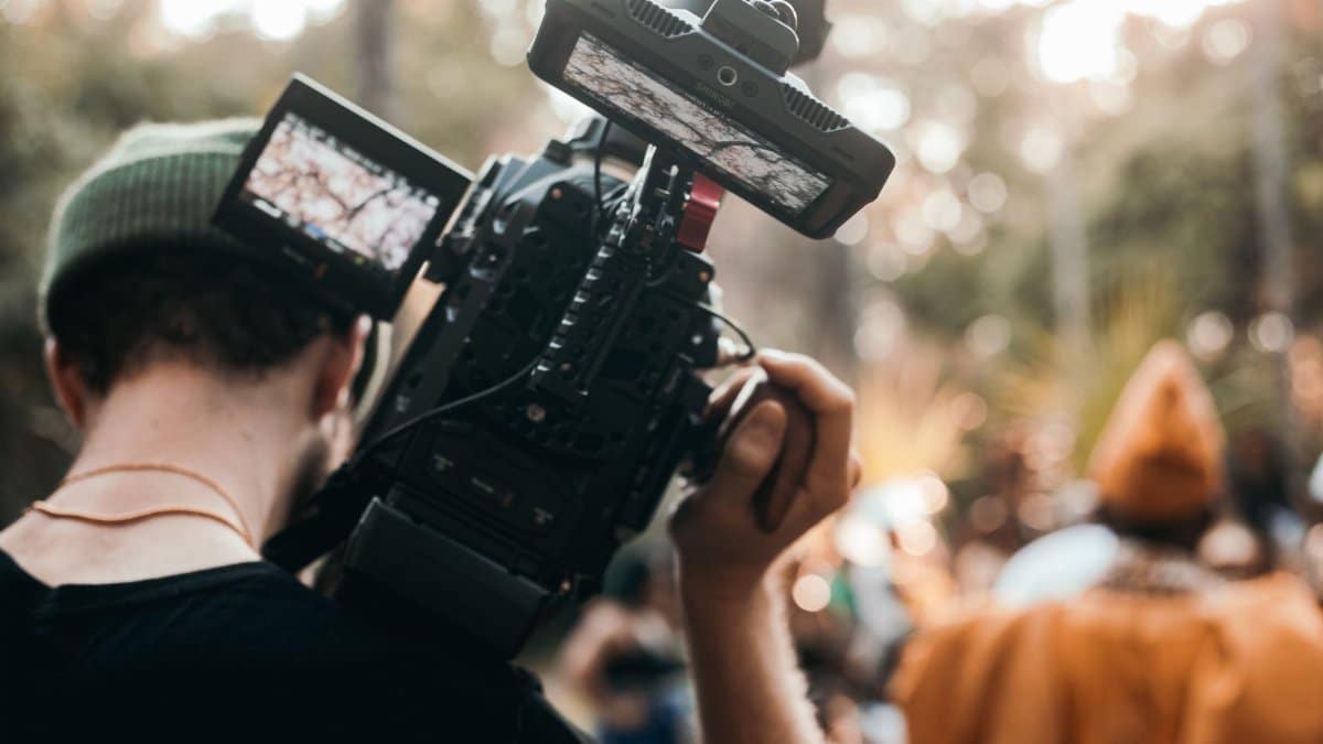 Man with a beanie filming an outdoor scene using professional camera equipment.