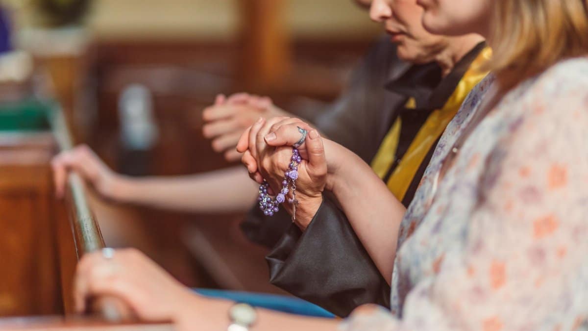Group of people praying with rosary beads in a church, conveying faith and spirituality.