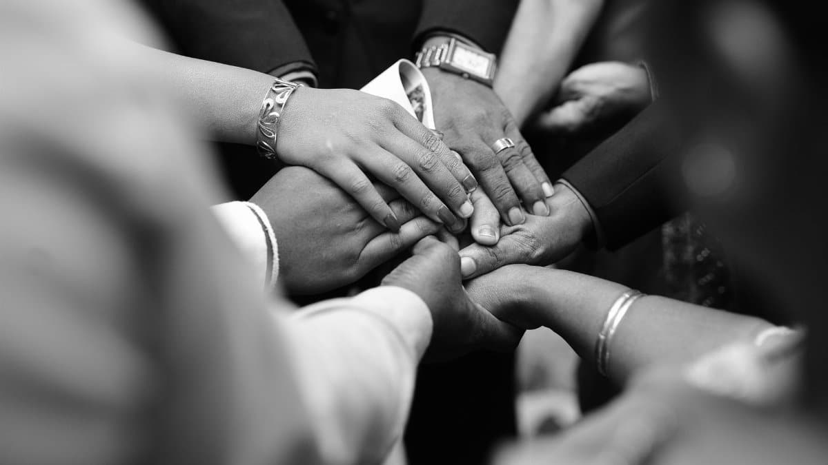 A close-up black and white photo of diverse hands united in prayer, symbolizing spiritual unity.